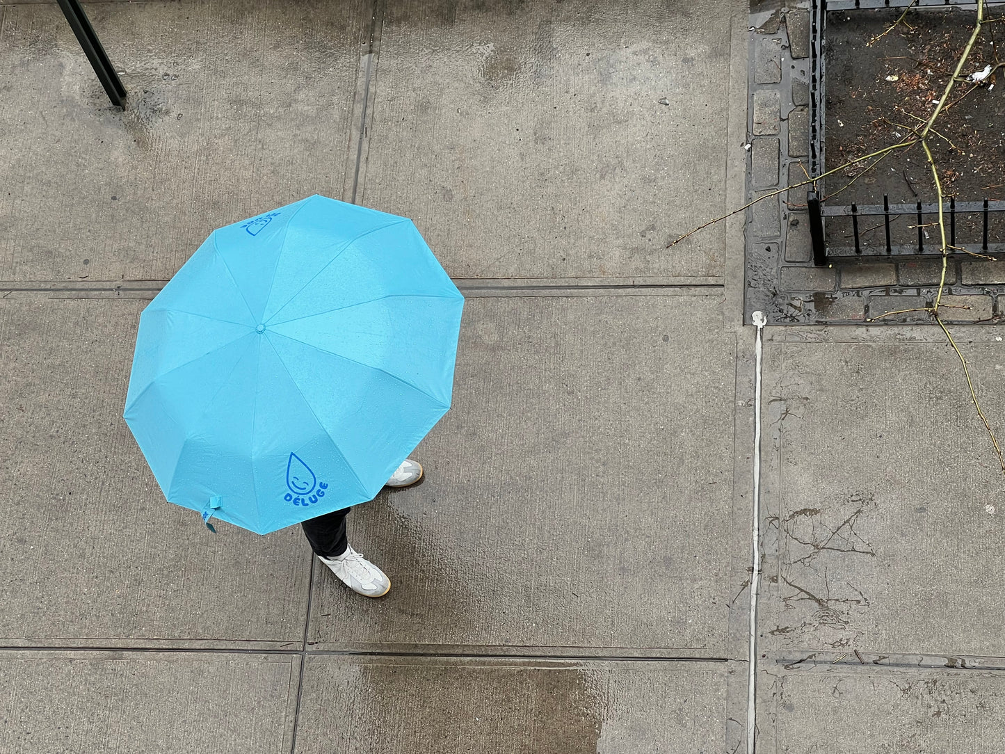 Person holding a blue umbrella on a sidewalk