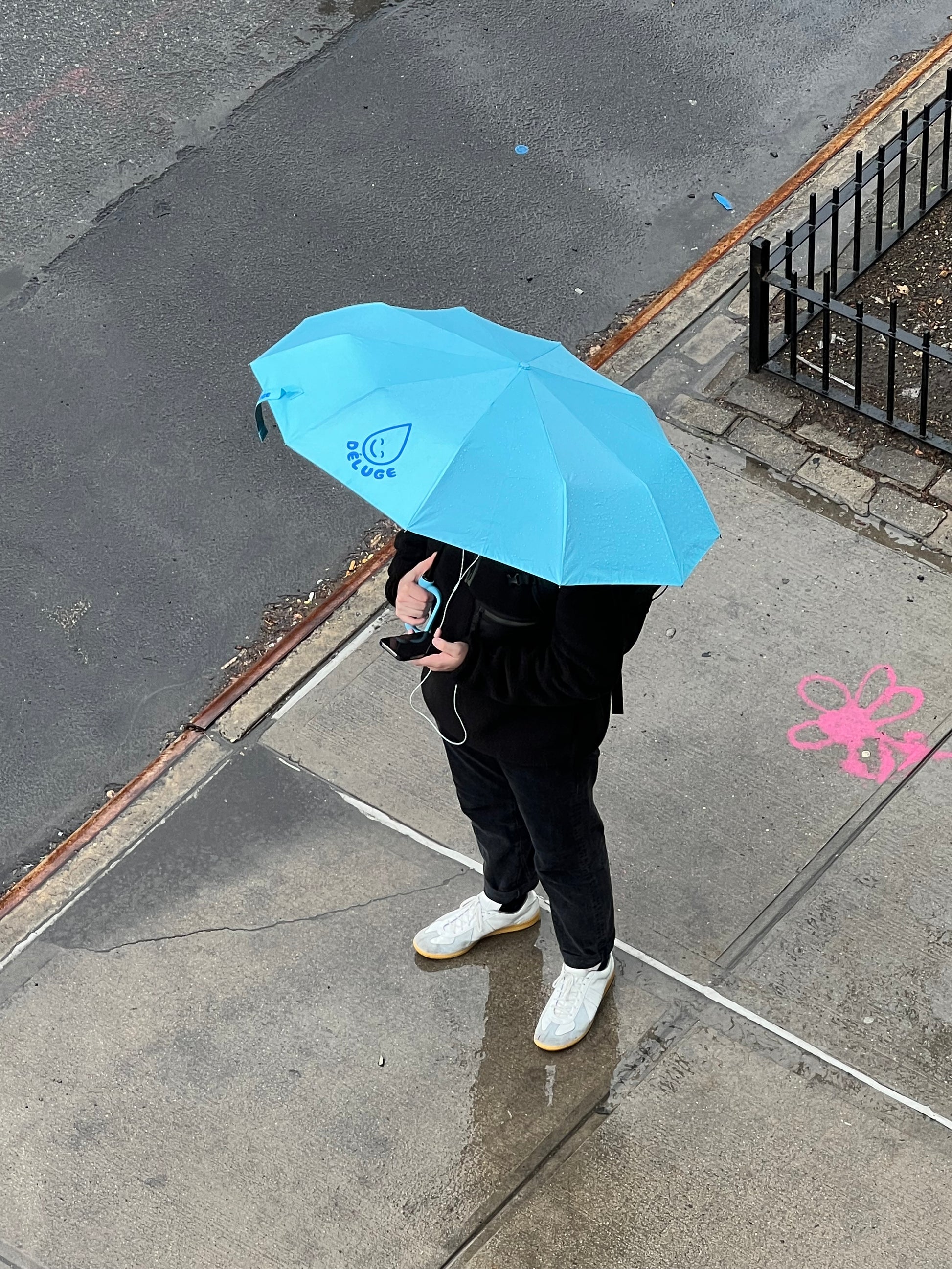 Person holding a blue umbrella on a sidewalk with pink graffiti.